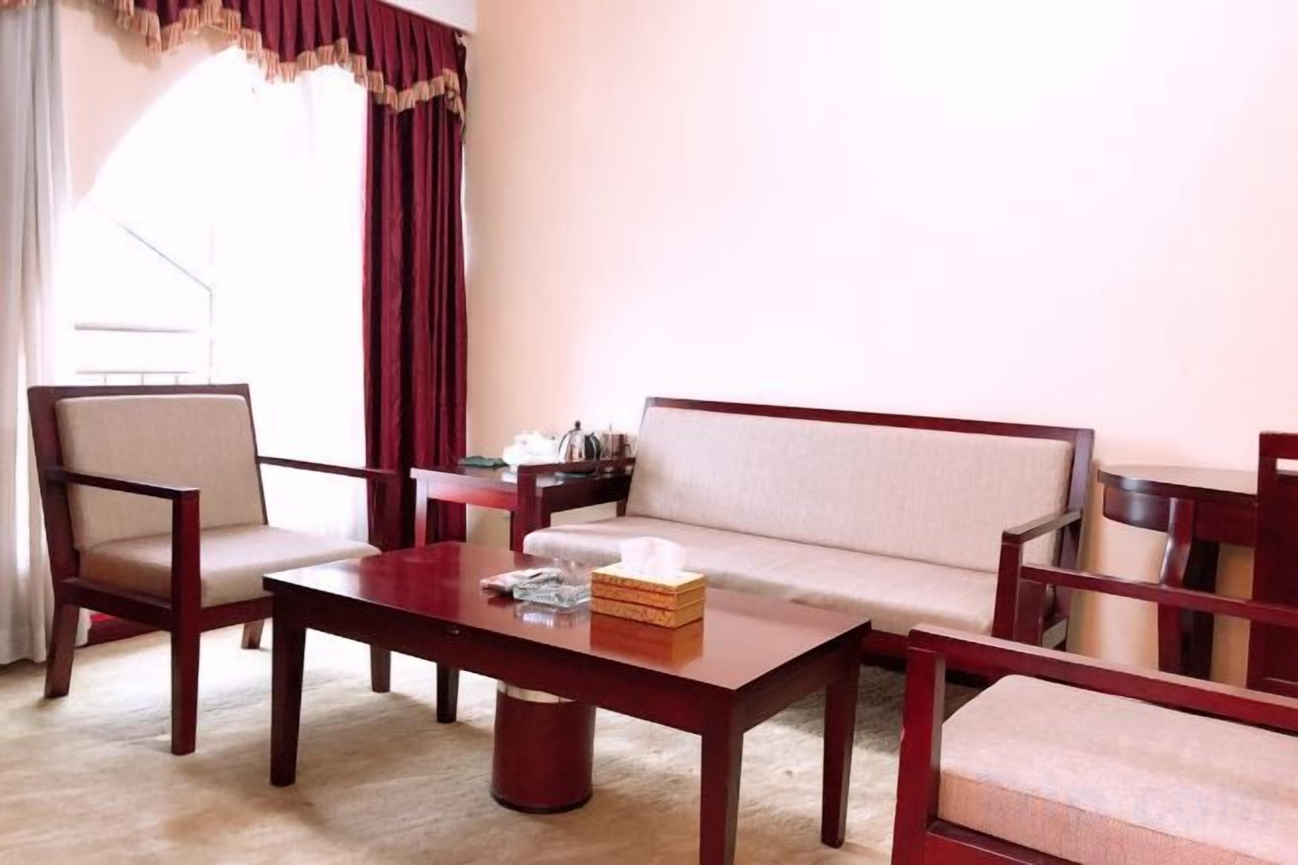 Una habitación con un sofá, dos sillones, una mesa de centro de madera y una mesita con una caja y una taza.