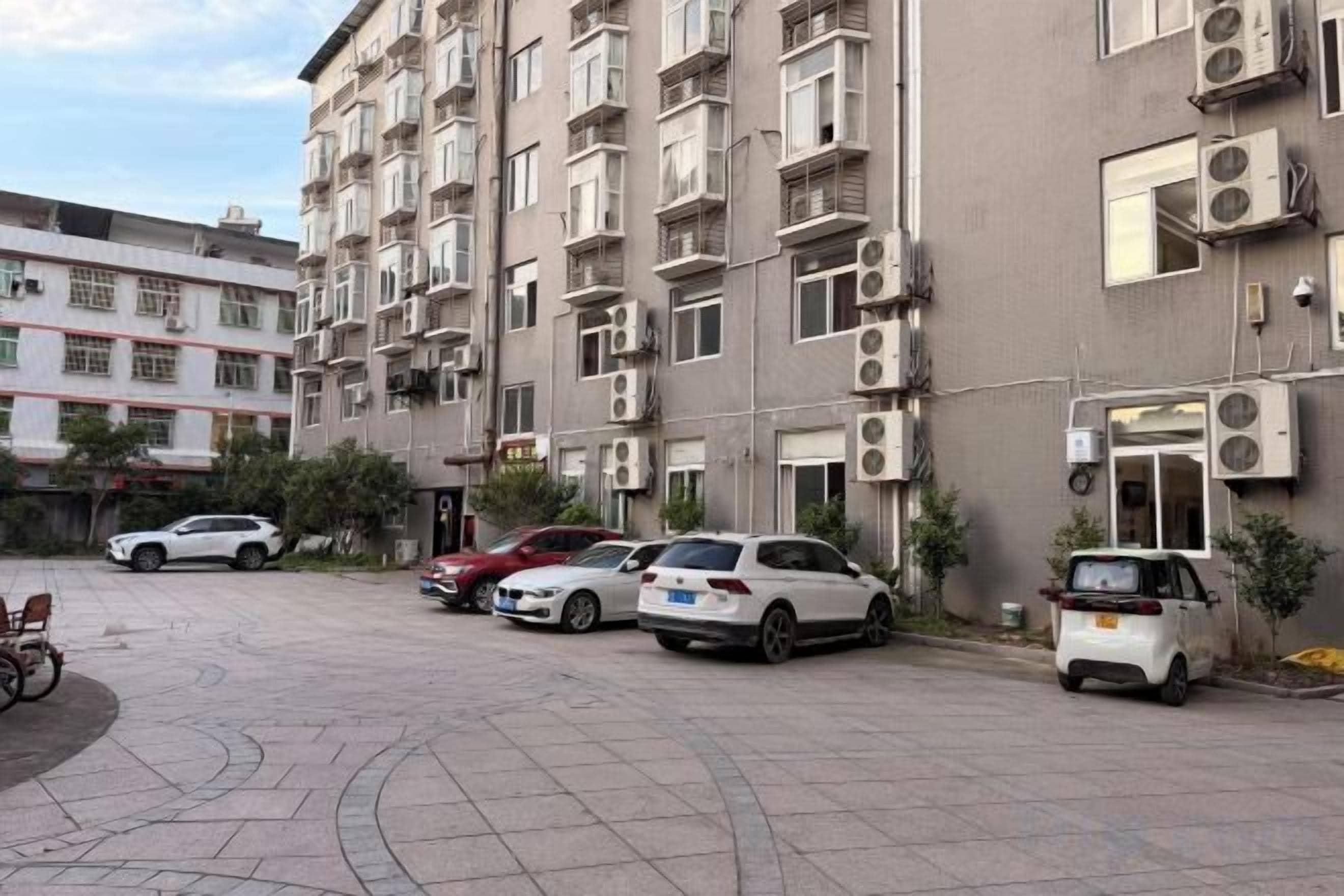 Un edificio residencial de varios pisos con aires acondicionados, coches aparcados y una bicicleta.