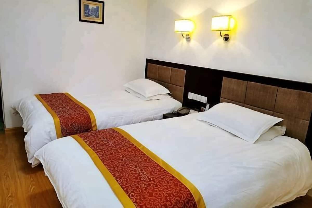 Two beds with white linens and red accents, a wooden floor, and wall-mounted light fixtures.