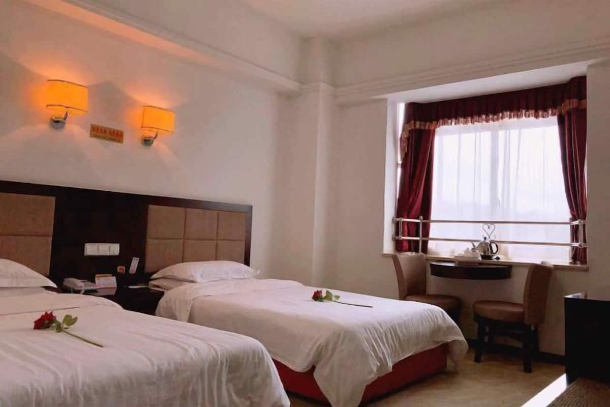 A hotel room with two beds, a desk, a chair, and a window with curtains.