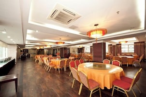 A spacious dining area with multiple round tables and chairs, a central chandelier, and an air conditioning unit on the ceiling.