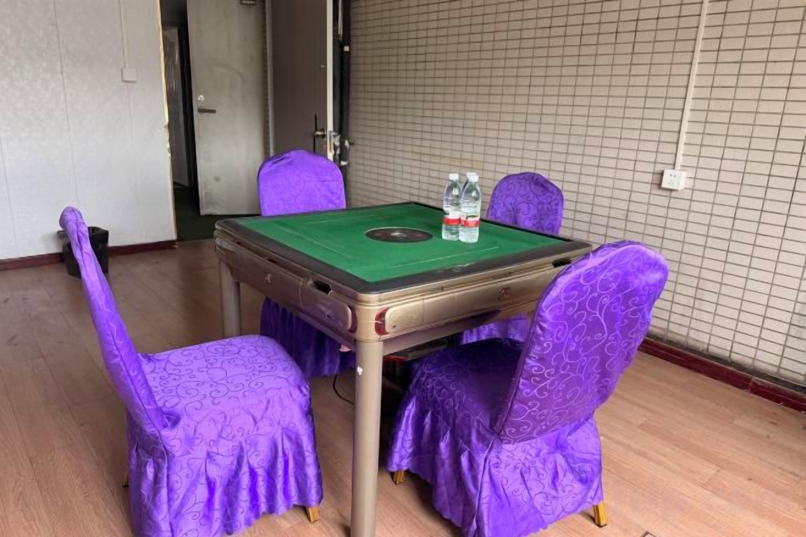 A room with a green felt table and chairs, two bottles of water, and a door to the left.
