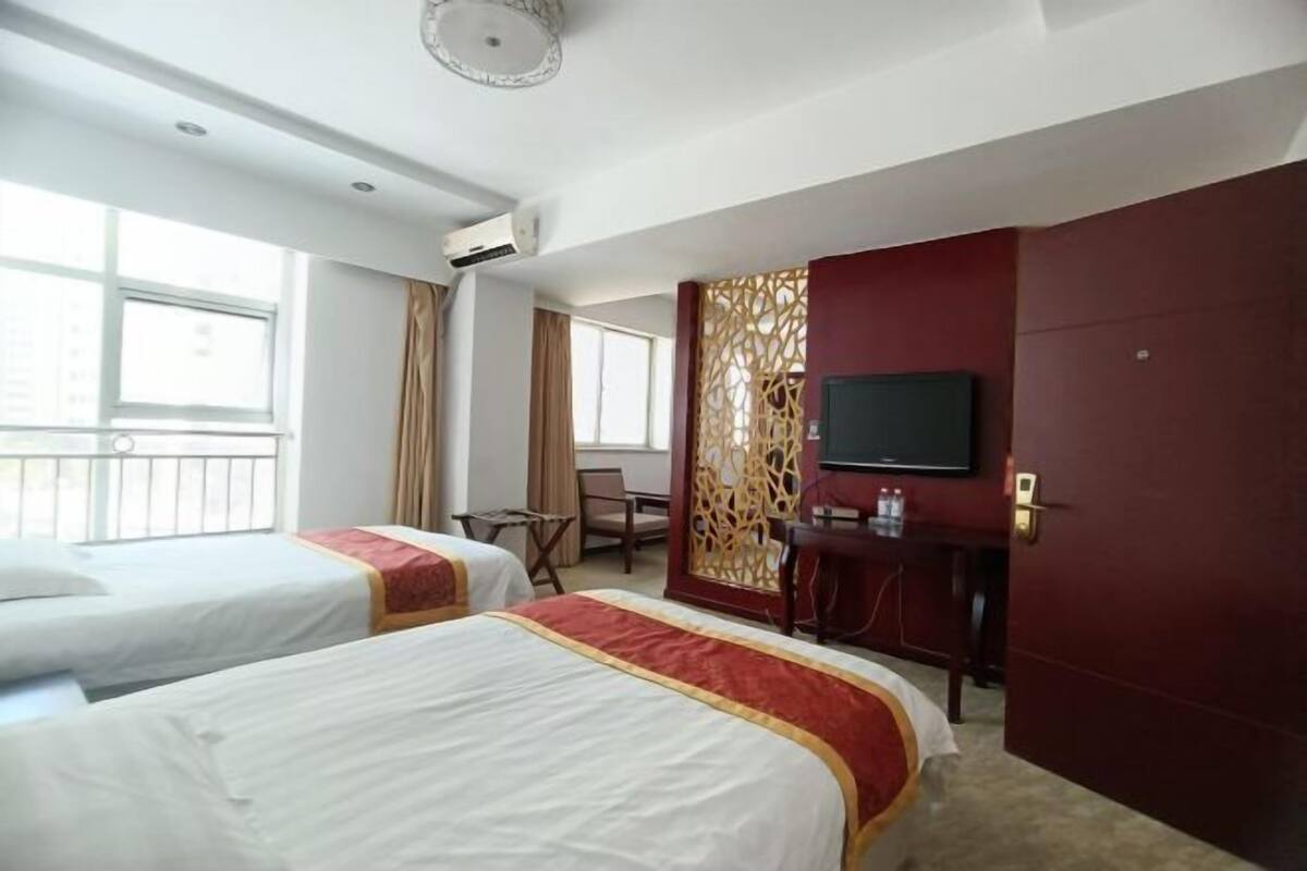 A hotel room with two beds, a TV, a desk with a chair, and a decorative partition.