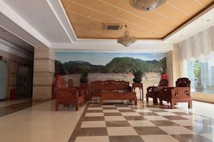 A lobby with a checkered floor, wooden furniture, a mural of a mountainous landscape, and a large window with curtains.