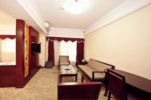 A hotel room with a sofa, a small table, a television, and a window with curtains.