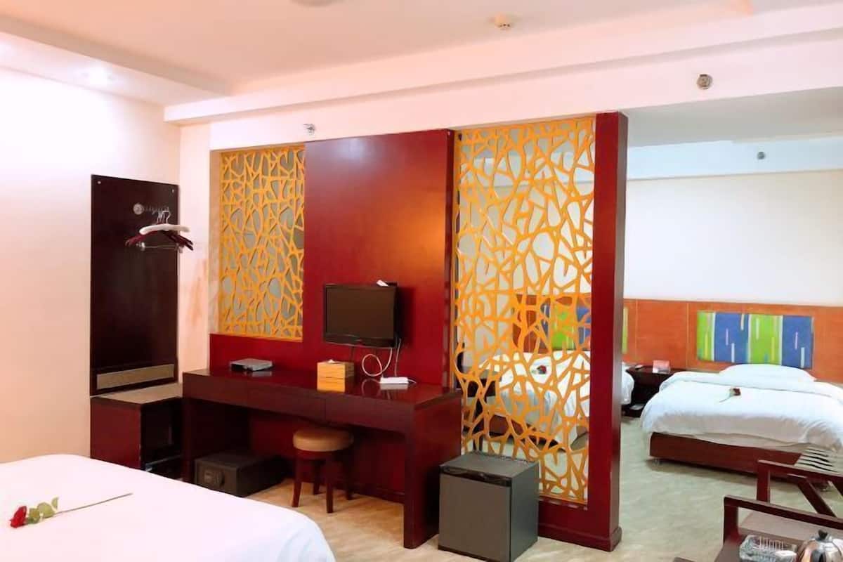 A hotel room with a bed, desk, TV, and a decorative partition.