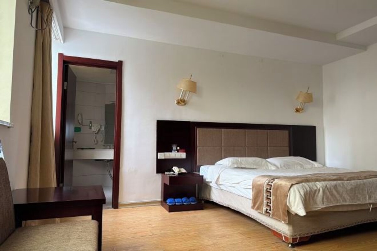 A hotel room with a bed, bedside table, lamp, and a view of the bathroom.