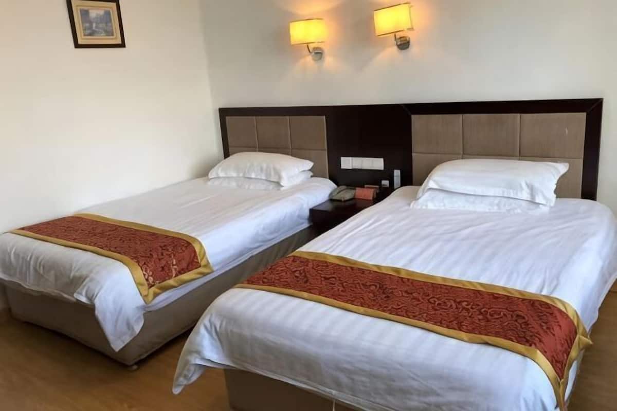 Two twin beds with white linens and red decorative borders, a wooden headboard, and two wall-mounted lamps.