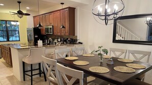Une cuisine moderne avec des meubles en bois, un îlot central et un coin repas comprenant une table en bois foncé et des chaises blanches.