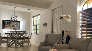 Un salon spacieux avec une table basse blanche, un canapé beige et un coin repas comprenant une table et des chaises en bois.