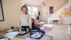 Un coin repas avec une table en bois dressée pour le repas, un escalier en arrière-plan et un salon avec un canapé et une table basse.