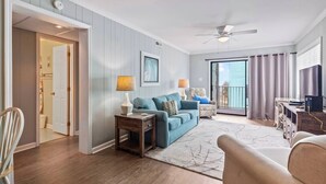 Ein Wohnzimmer mit einem blauen Sofa, einem Holztisch, einem Fernseher und einem Deckenventilator.