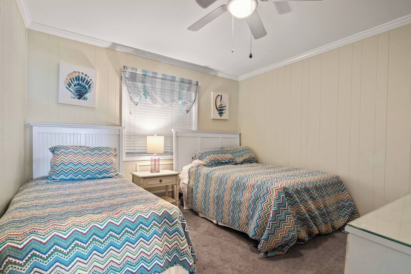 A bedroom with two beds, a nightstand, a ceiling fan, and a window with a curtain.