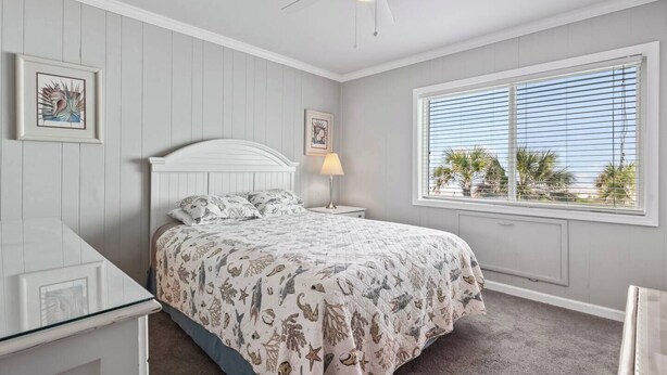 Ein Schlafzimmer mit einem Bett, einem Nachttisch, einer Lampe, einem Deckenventilator und einem Fenster mit Jalousien.