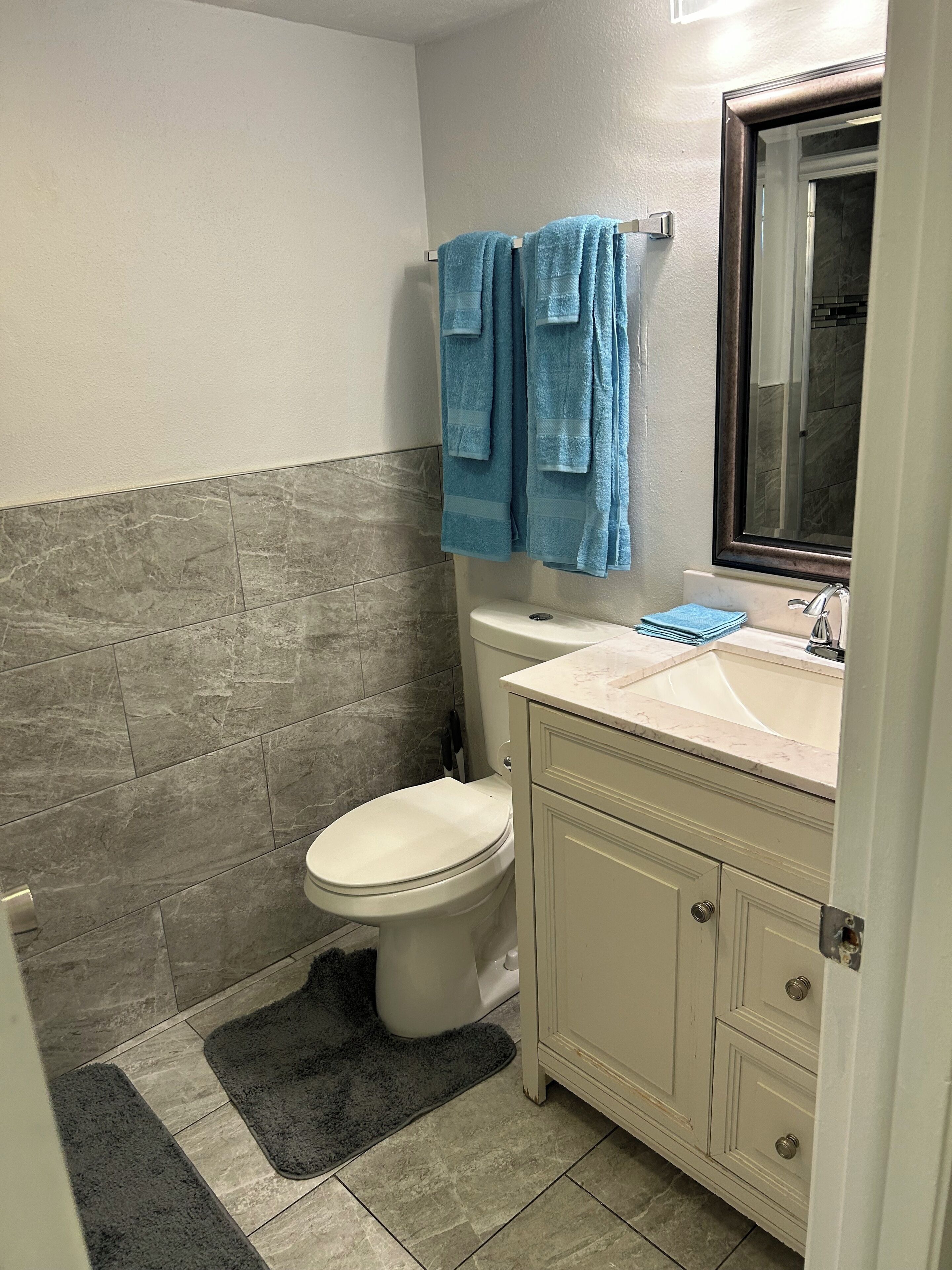 A bathroom with a toilet, sink, and mirror. There are towels hanging on a rack.