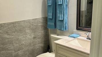 A bathroom with a toilet, sink, and mirror. There are towels hanging on a rack.