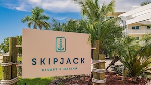 Señal para Skipjack Resort & Marina con un logotipo, rodeada de palmeras y una valla de madera.