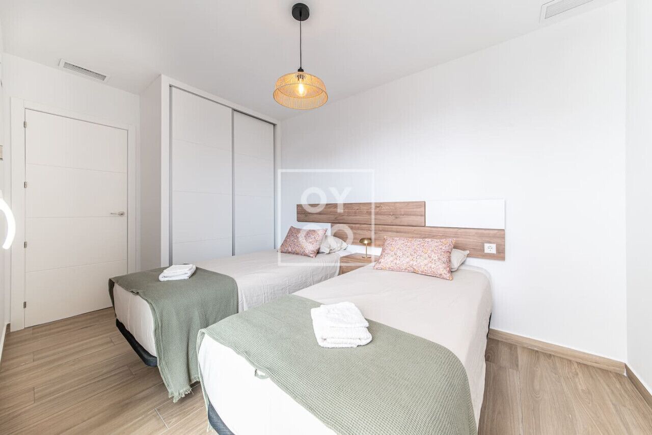 A modern hotel room with two single beds, a wooden headboard, a hanging light fixture, and a white door.