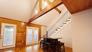 Une pièce spacieuse avec un plancher en bois, une table à manger avec des chaises, un escalier avec une rampe en métal et une porte avec des panneaux de verre.