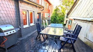 En udendørs terrasse med grill, et bord og stole.