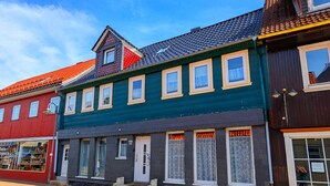 En række farverige bygninger med forskellige arkitektoniske stilarter, herunder en rød bygning med en butik til venstre og en mørkegrøn bygning med mange vinduer i midten.