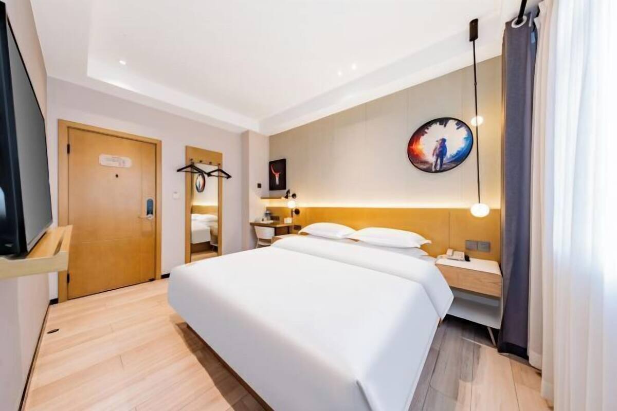 A hotel room with a bed, bedside table, TV, and a painting on the wall.