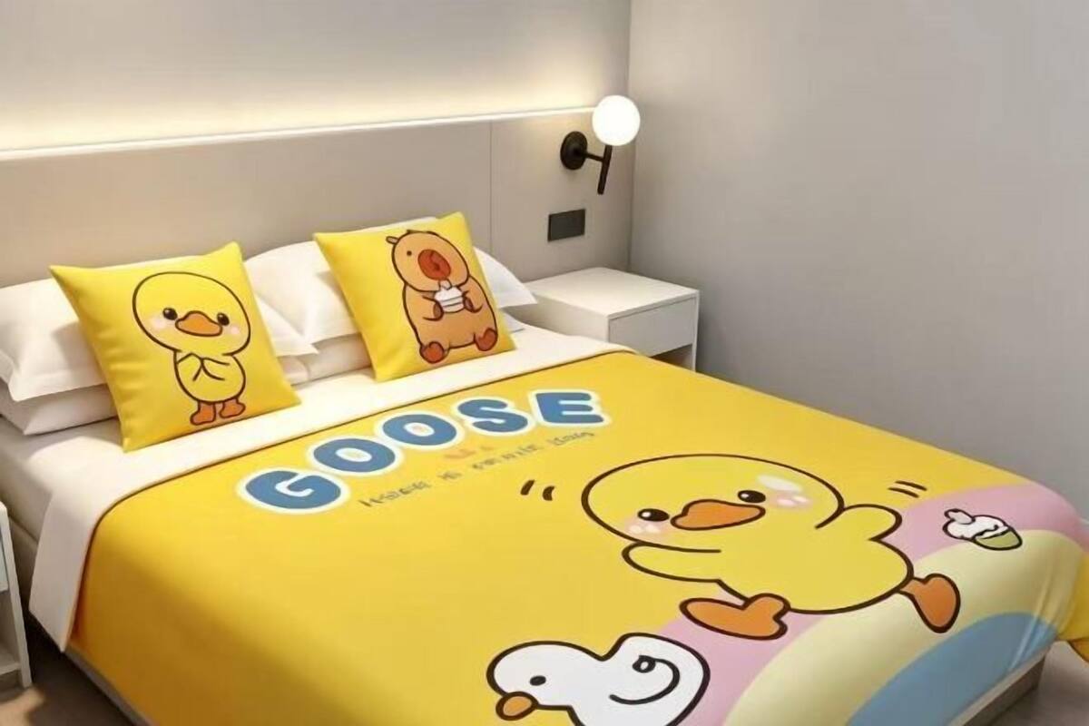 A bed with a goose-themed duvet, pillows, and wall-mounted light fixture.