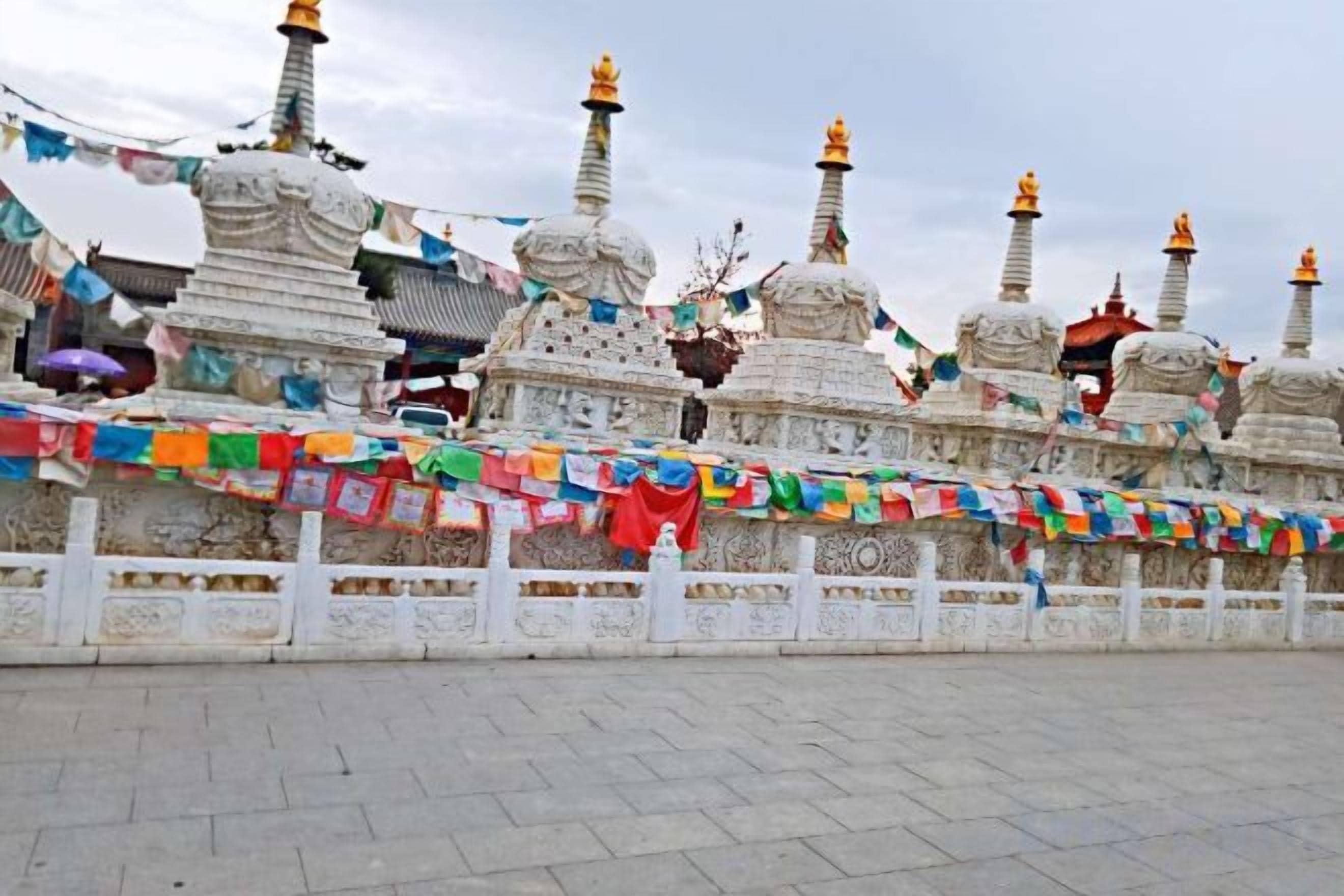 Eine Reihe weißer Stupas mit goldenen Spitzen, verziert mit bunten Gebetsfahnen.