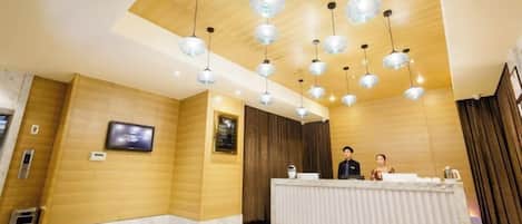 Zona de recepción de hotel con interior de madera, mostrador de recepción y múltiples lámparas colgantes.