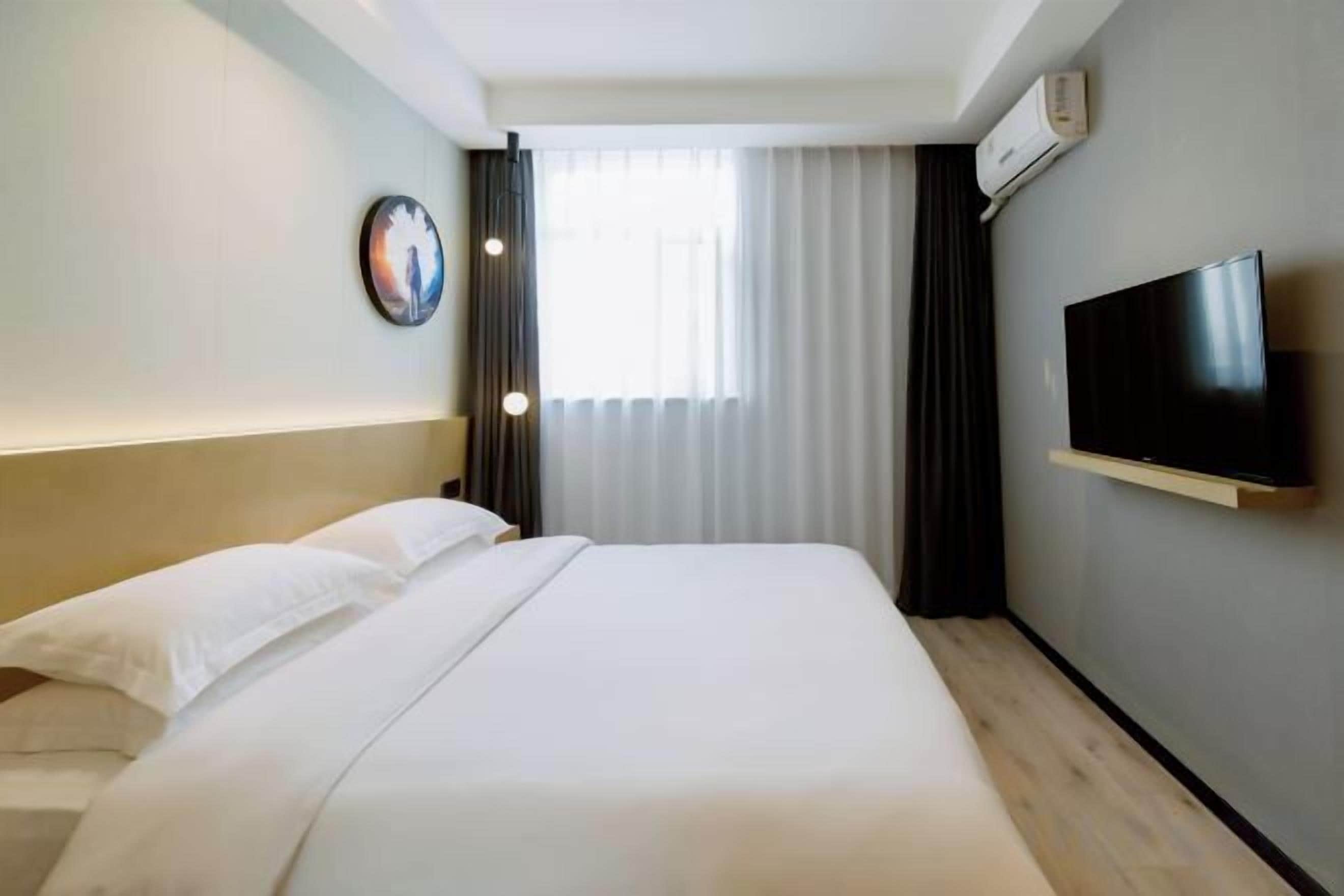 A hotel room with a bed, a television mounted on the wall, and a window with curtains.