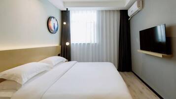 A hotel room with a bed, a television mounted on the wall, and a window with curtains.