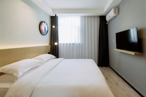 Una habitación de hotel con cama, televisor montado en la pared y ventana con cortinas.