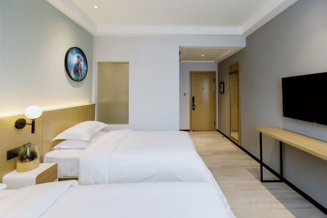 A hotel room with a bed, bedside table, lamp, and a TV mounted on the wall.