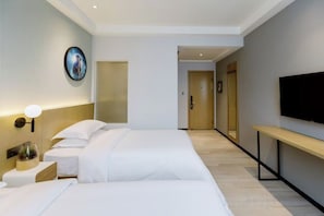 Una habitación de hotel con cama, mesita de noche, lámpara y televisor montado en la pared.