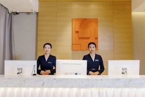 A reception desk with two staff members, a wooden wall with a geometric design, and a marble counter. - JIN YOTEL(South Second Ring & South Shiyangqiao Road, Hohhot) (Hohhot)