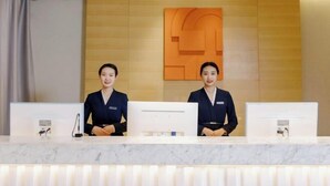 A reception desk with two staff members, a marble counter, and a wall-mounted digital display. - JIN YOTEL(South Second Ring & South Shiyangqiao Road, Hohhot) (Hohhot)