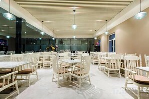 Un comedor espacioso con varias mesas y sillas, un diseño de techo moderno y ventanas amplias.