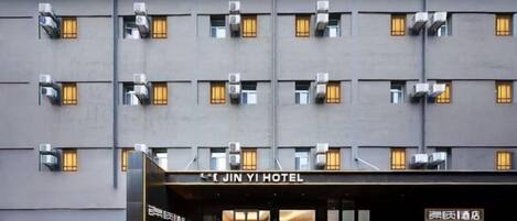 Un hotel moderno con varios pisos, unidades de aire acondicionado y una entrada destacada con puertas de vidrio.