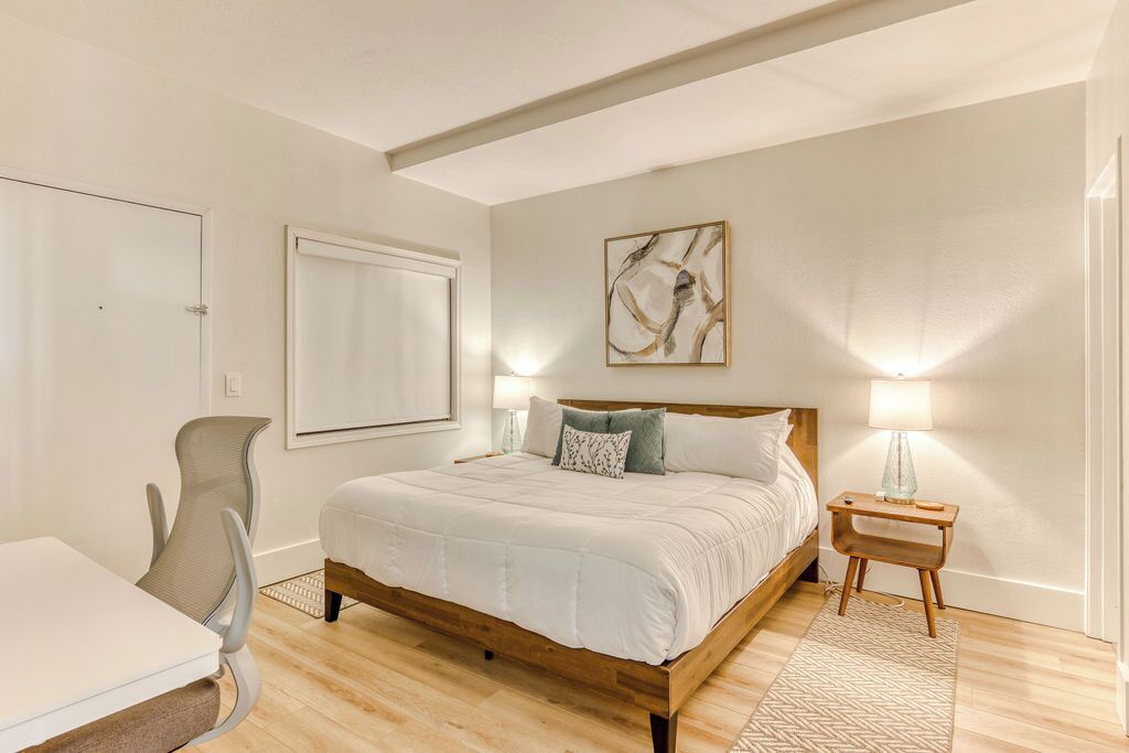 Une chambre à coucher avec un lit en bois, un bureau et une chaise. Un tableau est accroché au mur, et il y a deux lampes de chevet.