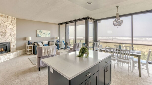 A modern kitchen with a large island, a stone fireplace, and a view of the beach. - The Sand & Sea Condos - Oceanfront (Seaside)