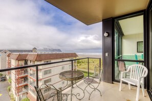 A balcony with a table and chairs, overlooking a beach and buildings. - The Sand & Sea Condos - Oceanfront (Seaside)