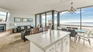 Un vaste espace de vie doté d’une grande fenêtre donnant sur la plage, d’une cheminée et d’un coin repas avec vue.