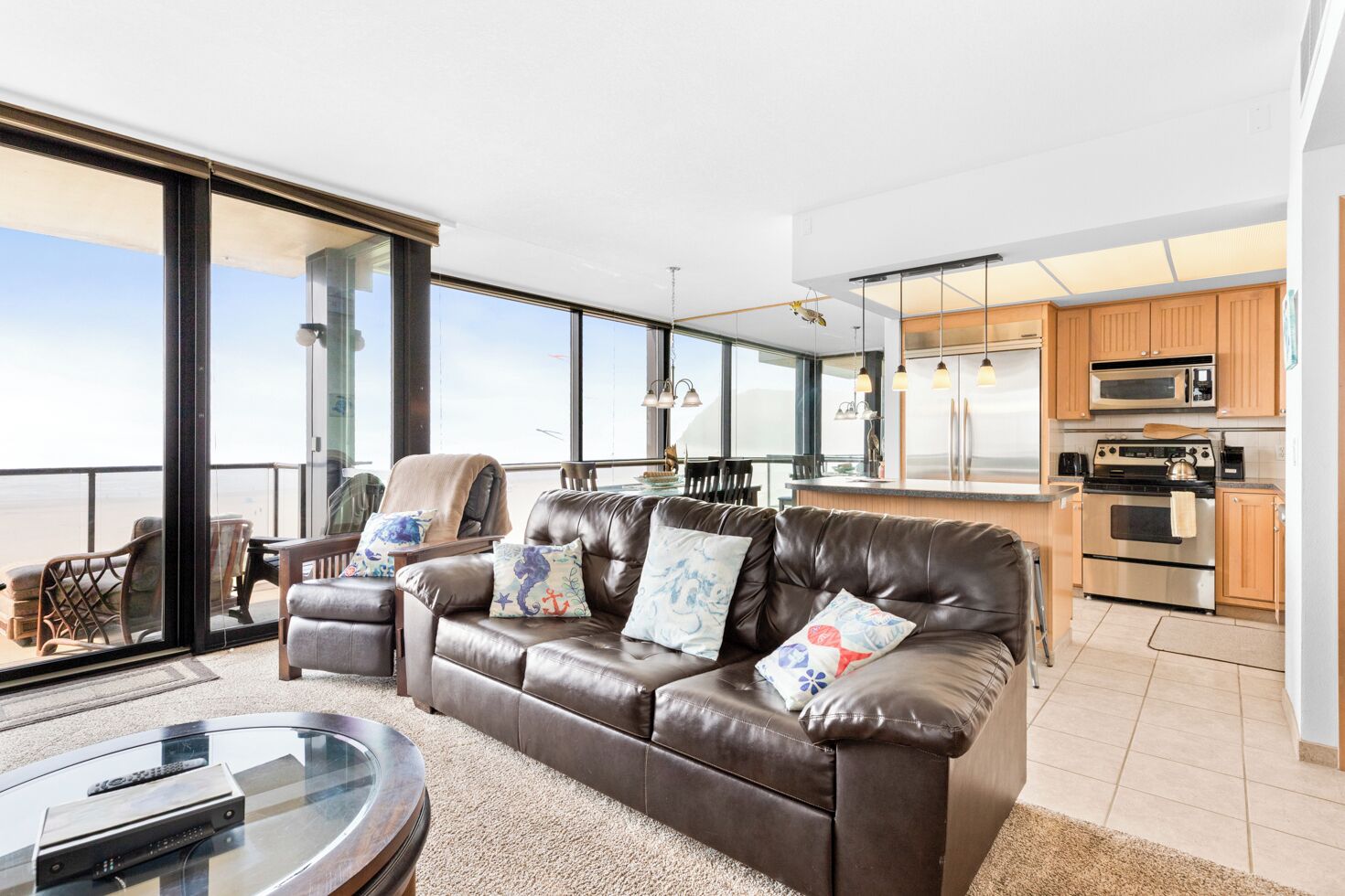 A modern living room with a leather sofa, a glass coffee table, and a view of the ocean.