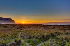 A coastal landscape with a sunset, grassy dunes, and a distant hill. - The Sand & Sea Condos - Oceanfront (Seaside)