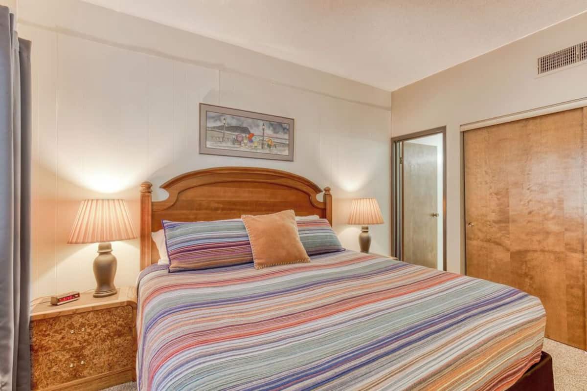 Un letto rifatto con una coperta a righe, due lampade ai lati e un quadro appeso alla parete.