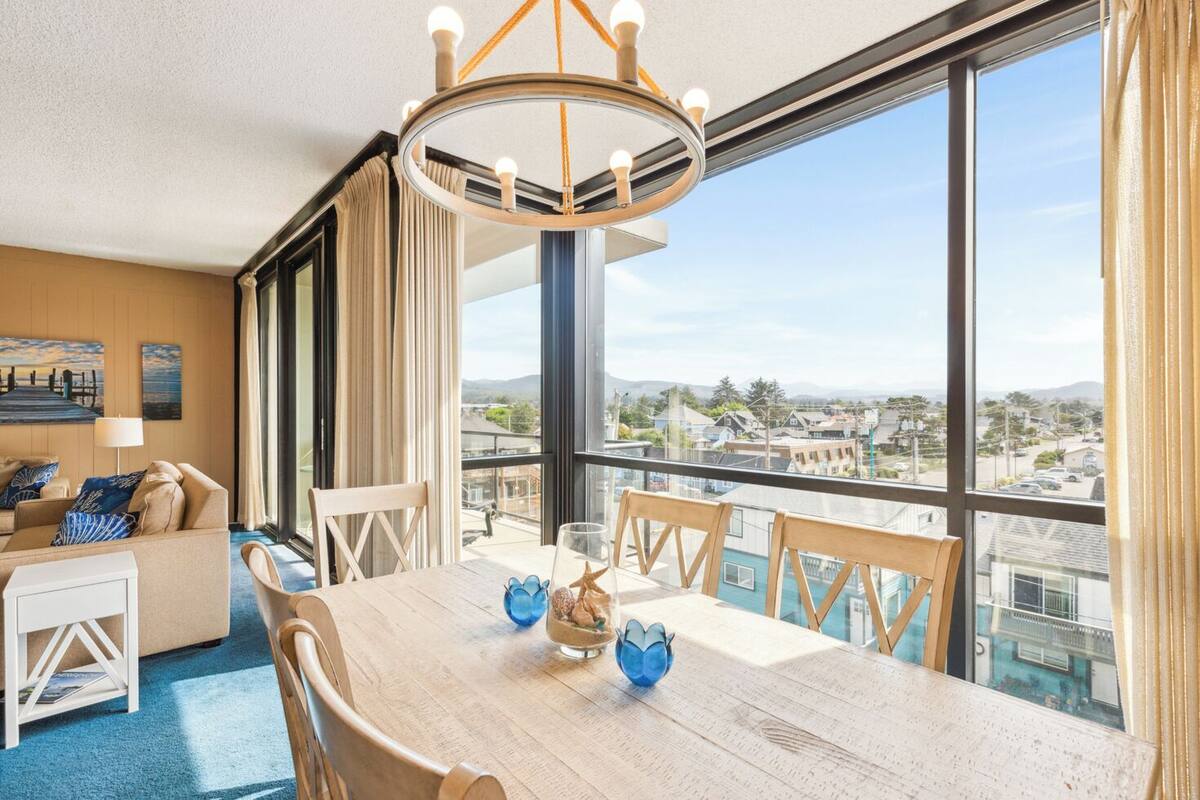 Una camera d'albergo moderna con un ampio balcone, un tavolo da pranzo con sedie e vista sulla città.