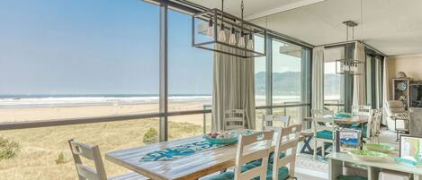 Un espace repas avec vue sur la plage, de grandes fenêtres et un lustre moderne.