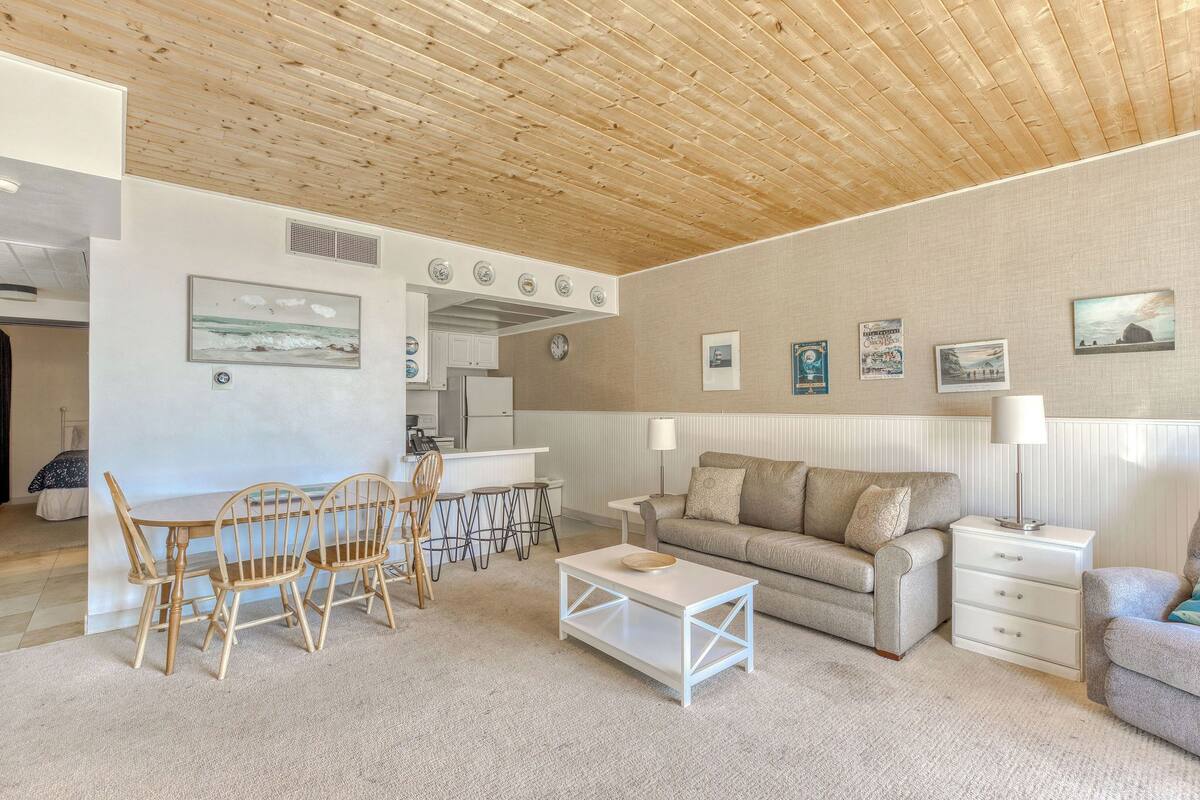 Un soggiorno moderno con soffitto in legno, una zona pranzo con sedie in legno, un divano e un tavolino.