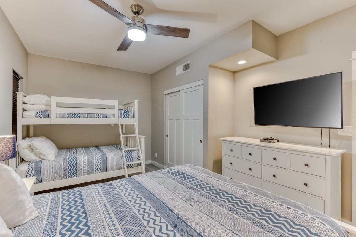 Camera da letto con letti a castello, ventilatore a soffitto, televisore e cassettiera.