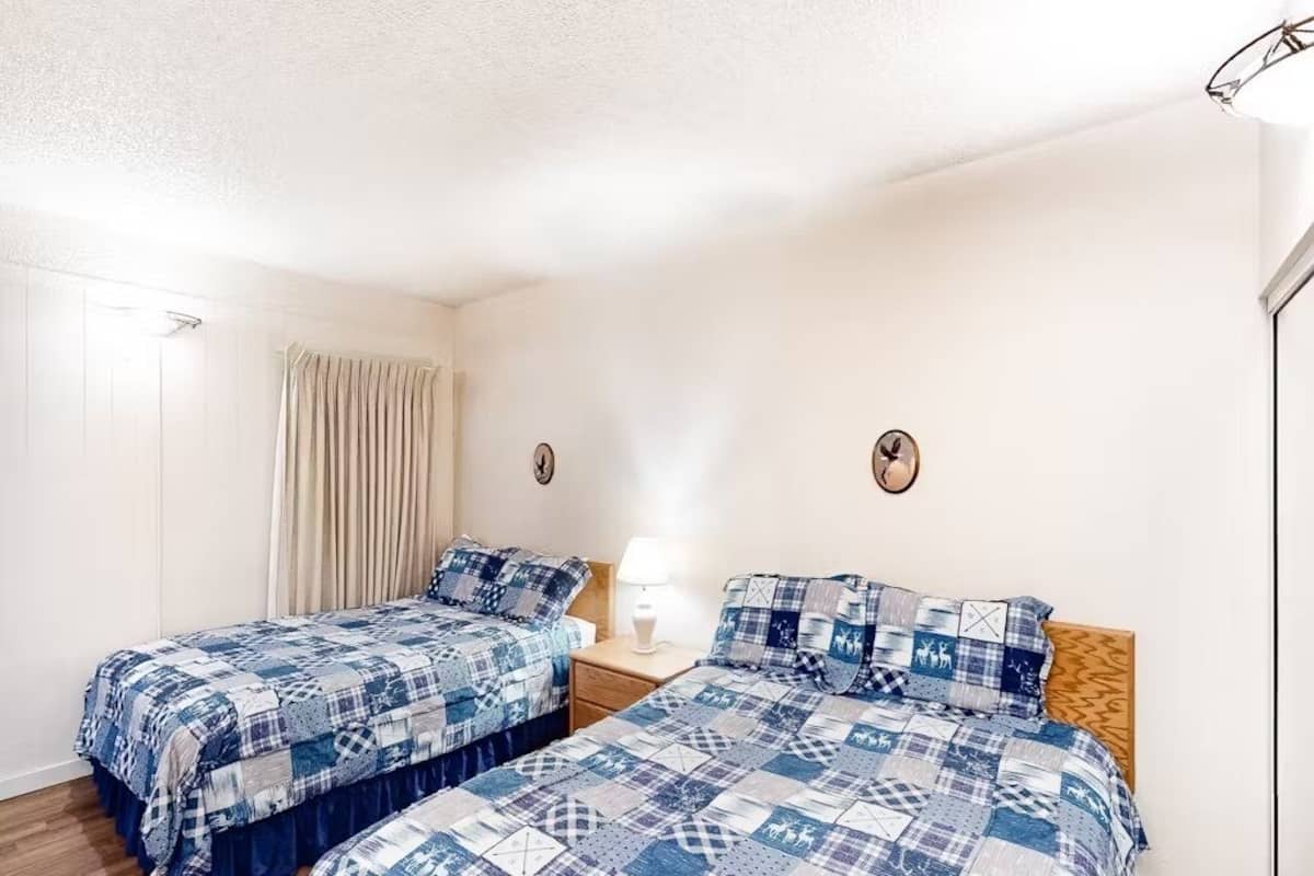 Camera da letto con due letti, ognuno con copriletto bianco e blu a quadretti, una testiera in legno e un comodino con una lampada.